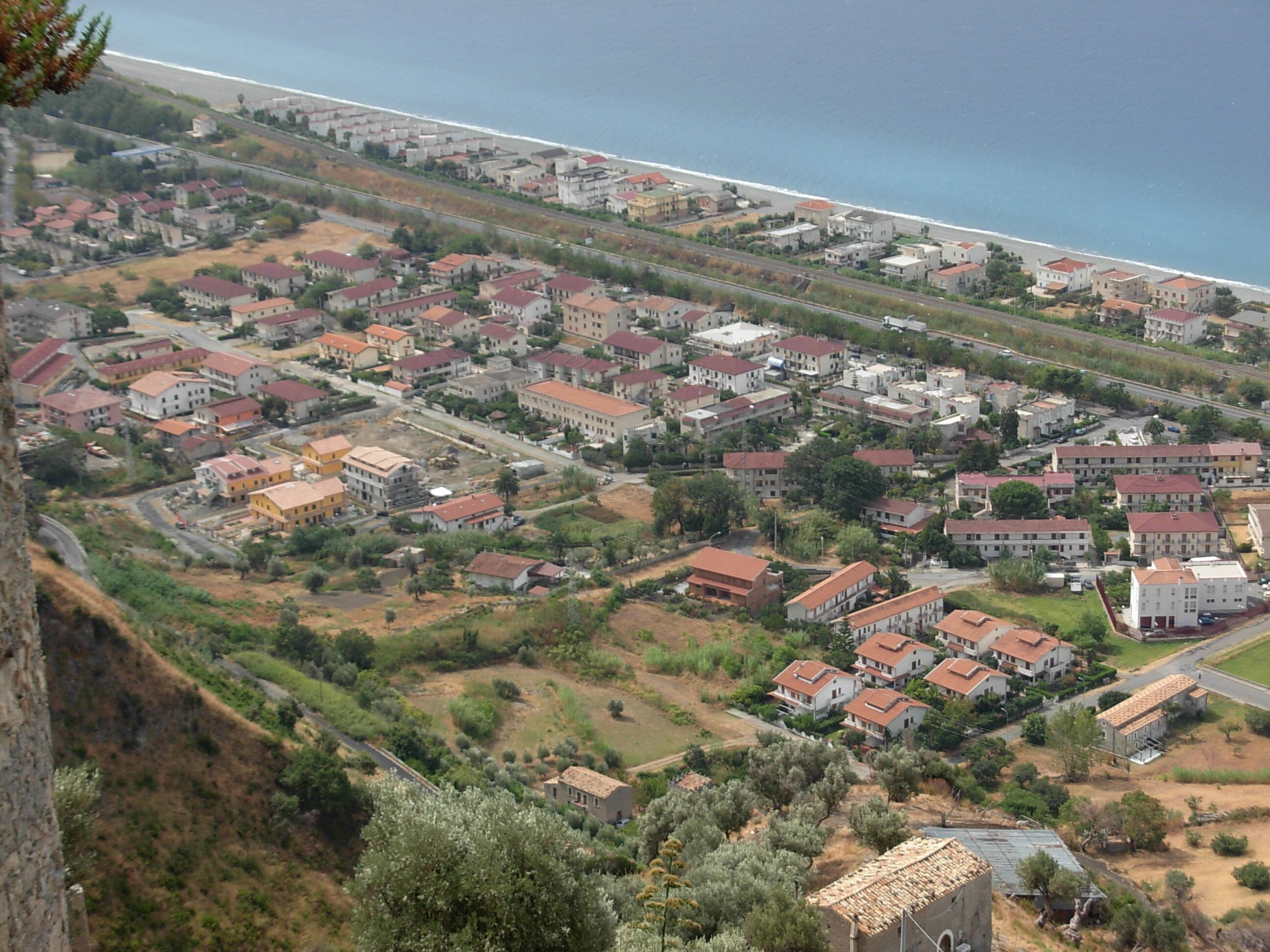 A coastal residential area with houses along the beach and a hilly landscape in the background.