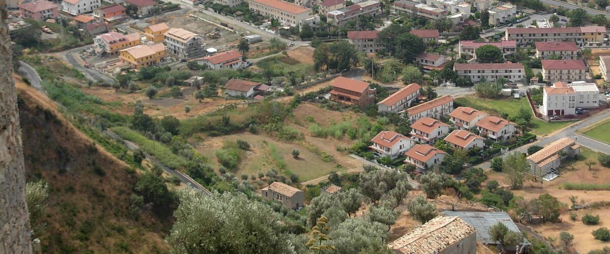 A coastal residential area with houses along the beach and a hilly landscape in the background.