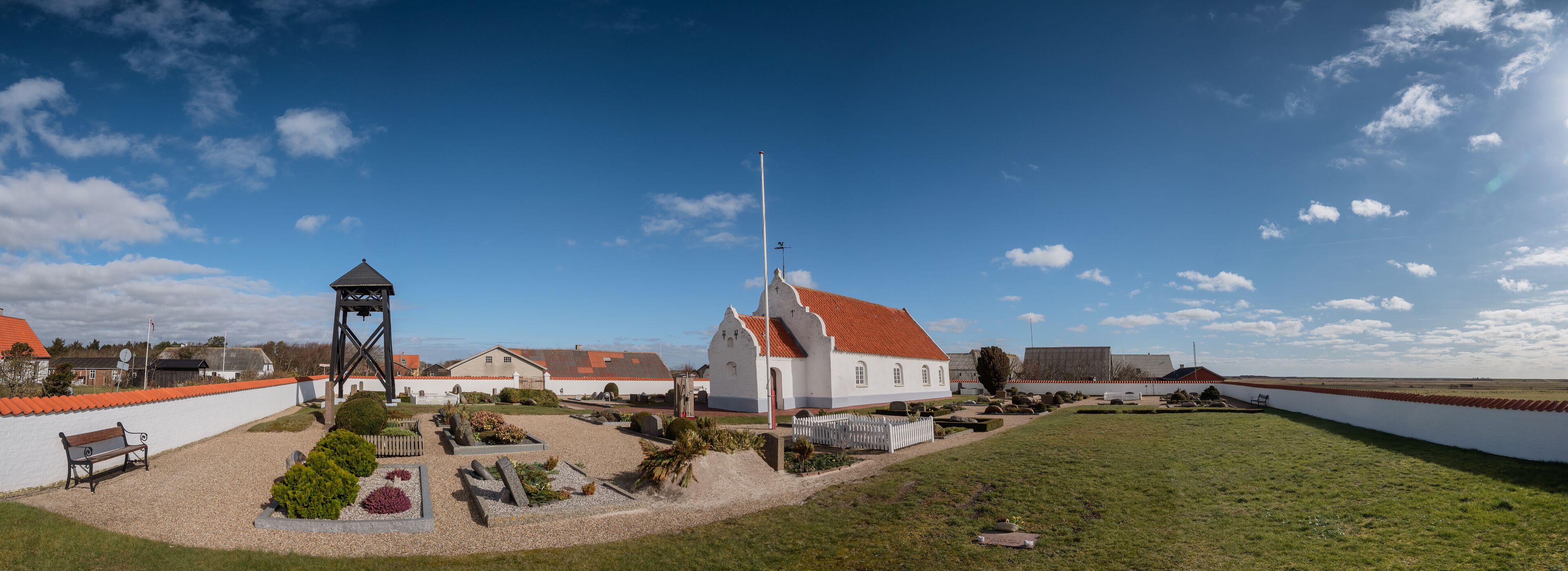 A church with a red roof, a bell tower, and a white fence surrounding a cemetery.