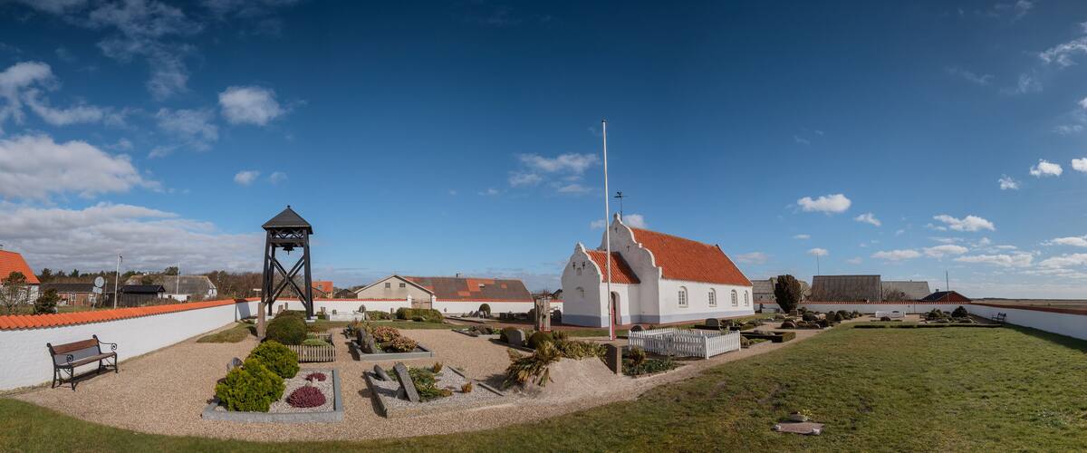 A church with a red roof, a bell tower, and a white fence surrounding a cemetery.