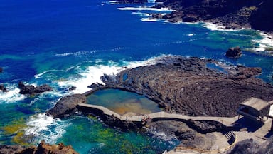 A coastal landscape with rocky cliffs, clear blue waters, and a small man-made pool surrounded by a stone walkway.