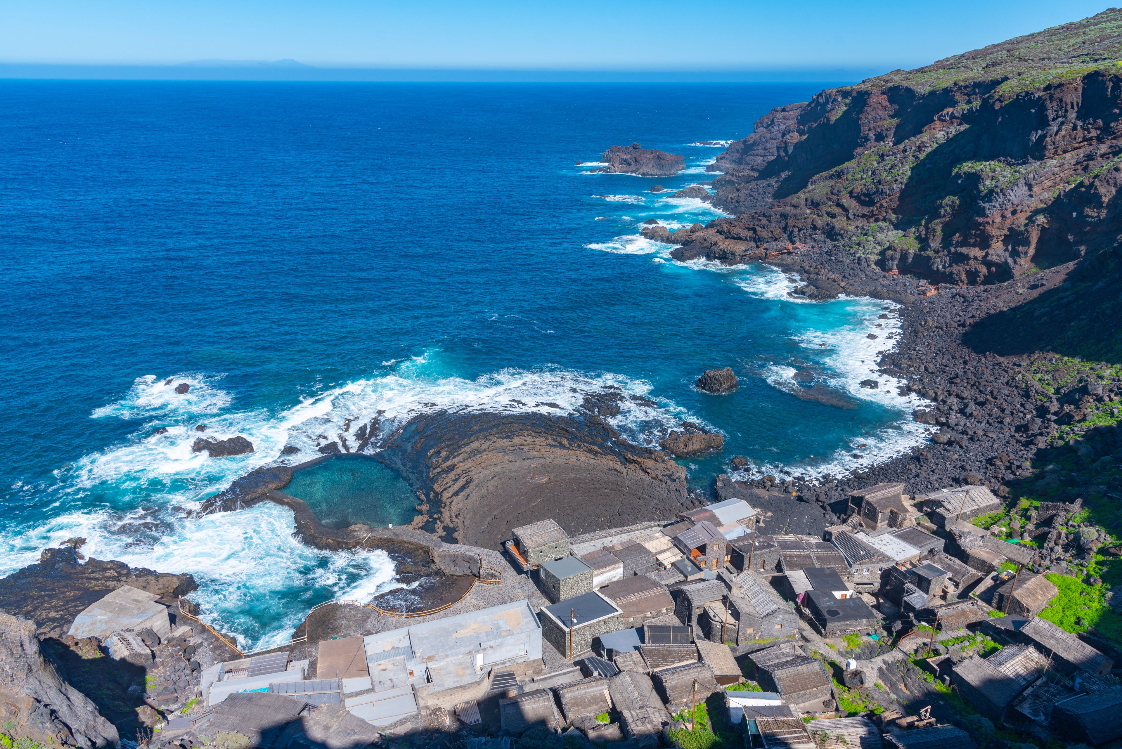 A coastal village with traditional stone buildings, a rocky shoreline, and the ocean.