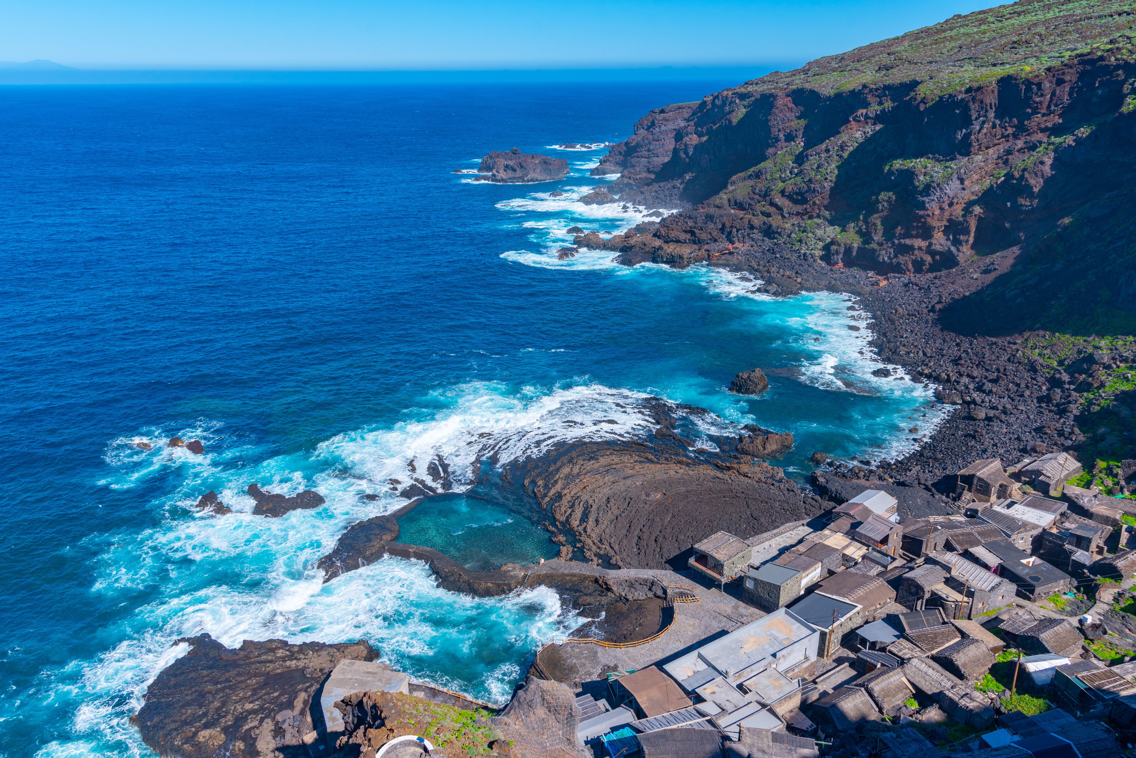 A coastal village with traditional stone buildings, rocky cliffs, and the ocean.