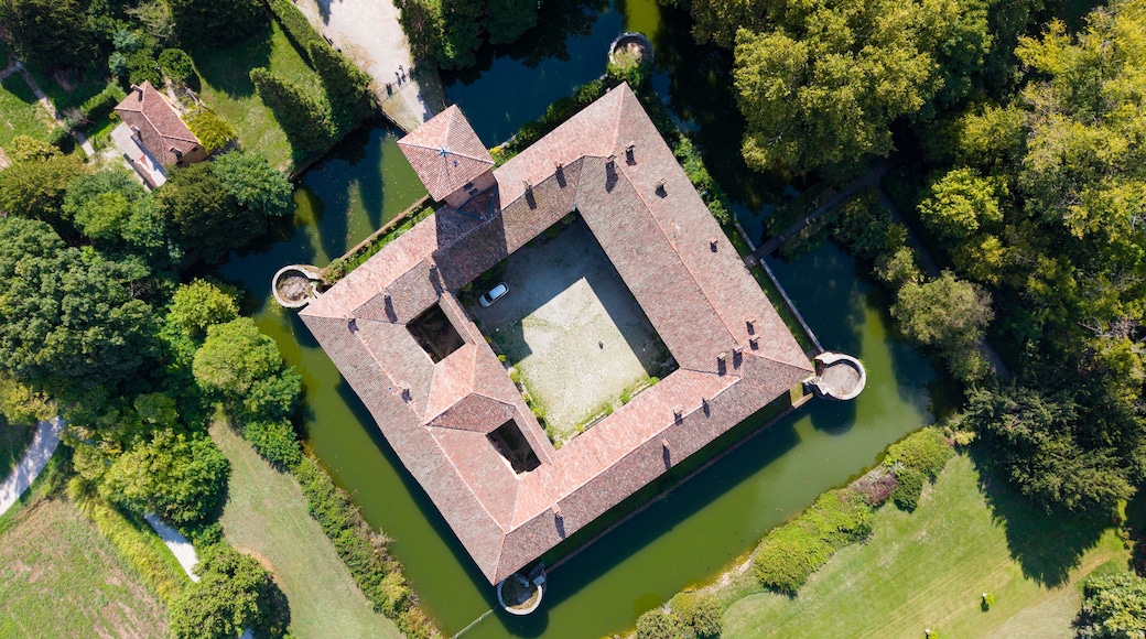 An aerial view of a square-shaped fortress with a moat surrounding it, set in a lush green landscape.