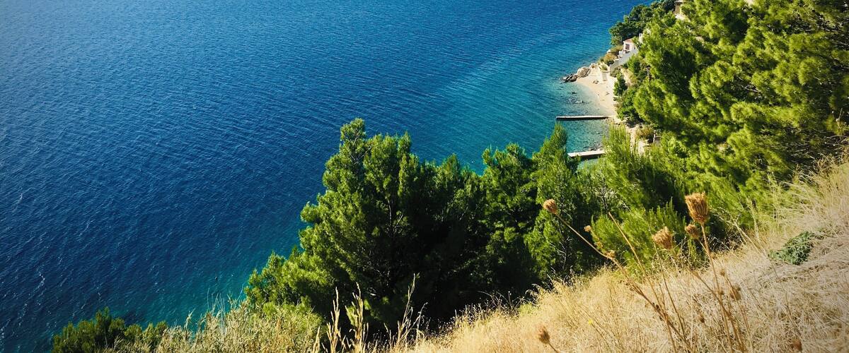 A coastal landscape with a clear blue sea, a boat in the distance, and a small building near the shore.