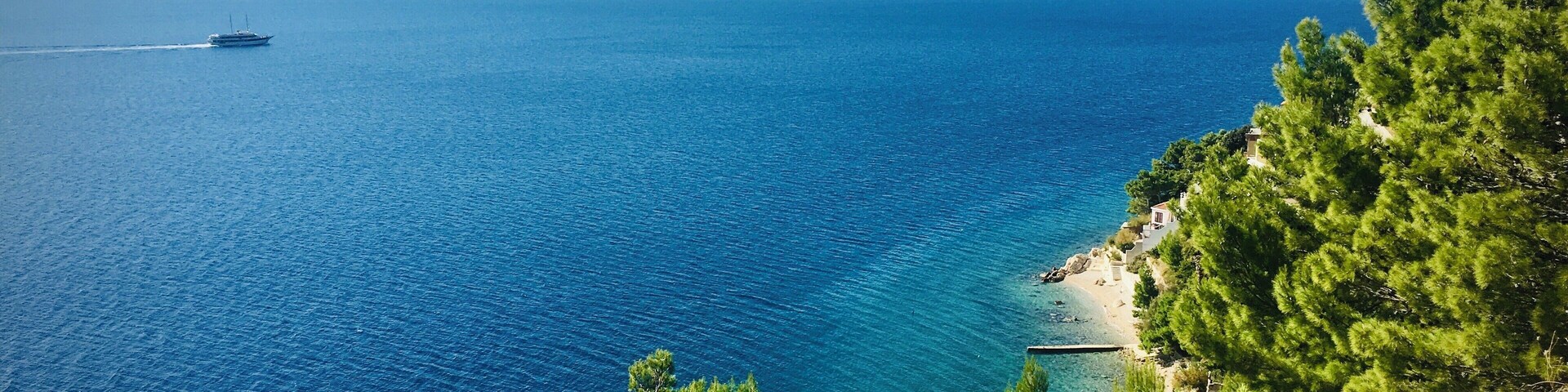 A coastal landscape with a clear blue sea, a boat in the distance, and a small building near the shore.