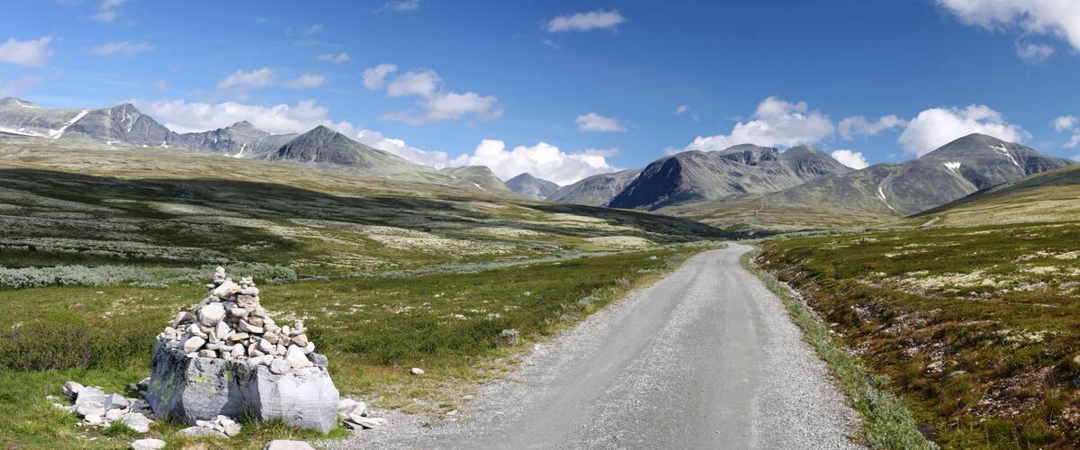 A gravel road leading through a mountainous landscape with a cairn in the foreground.