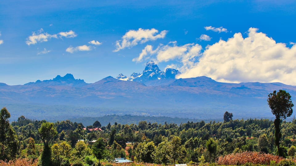 A mountainous landscape with a clear sky, a prominent peak, and a valley with scattered trees and buildings.