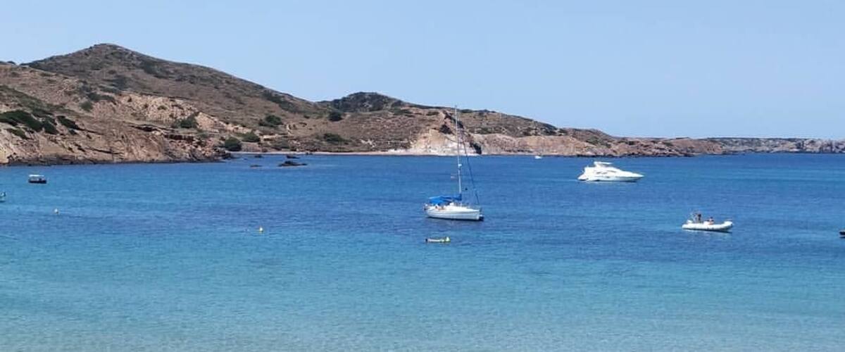 A clear coastal scene with a rocky shoreline, calm blue waters, and a few boats.