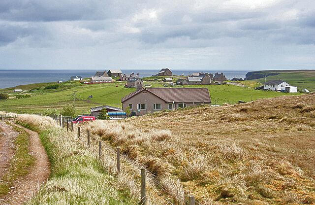 A coastal village with houses, a dirt path, and the sea in the background.
