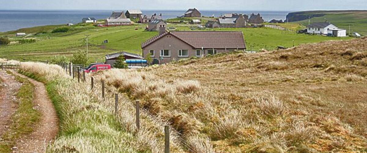 A coastal village with houses, a dirt path, and the sea in the background.