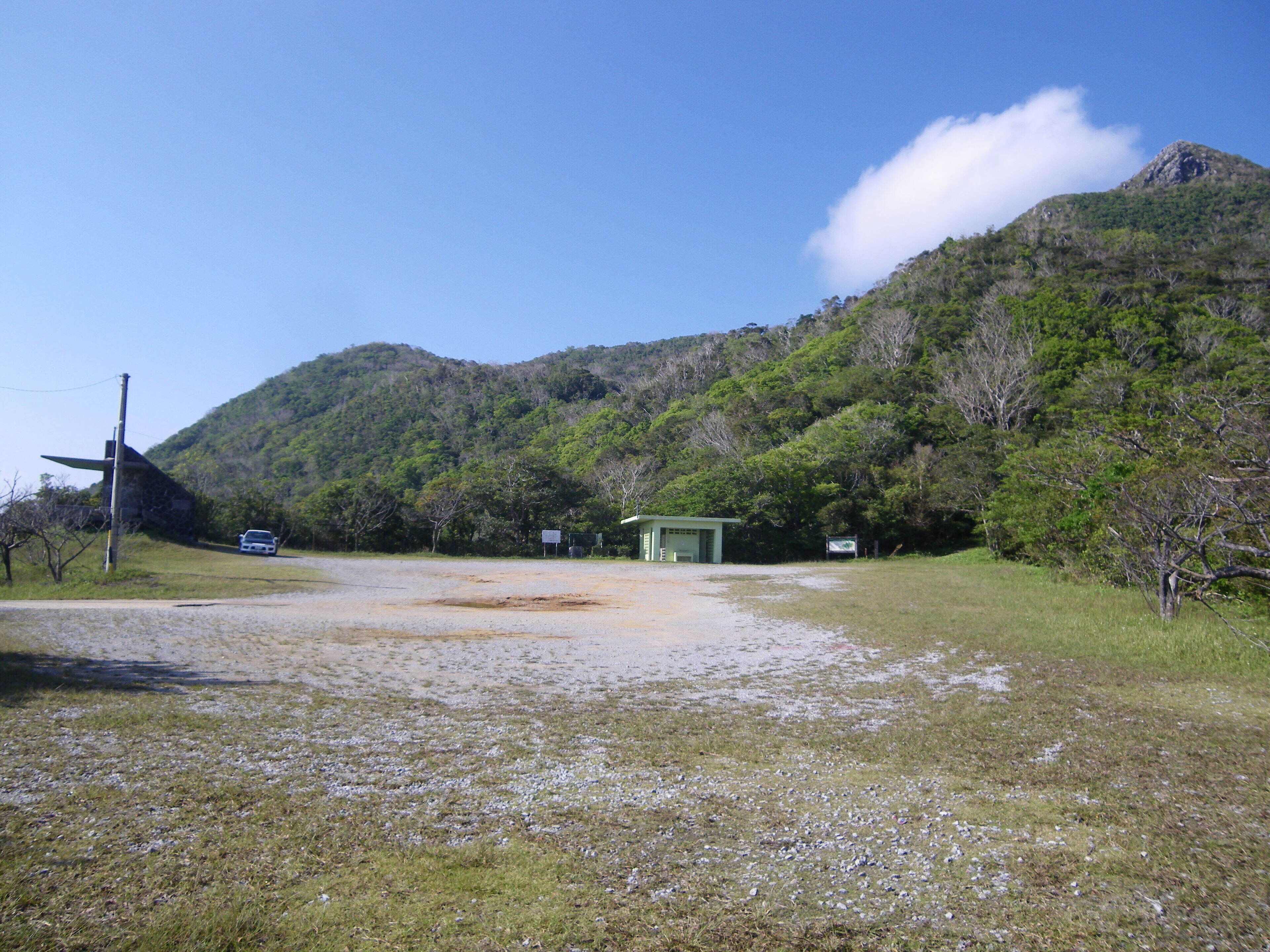 A rural landscape with a gravel road, a small building, and a car parked on the side.