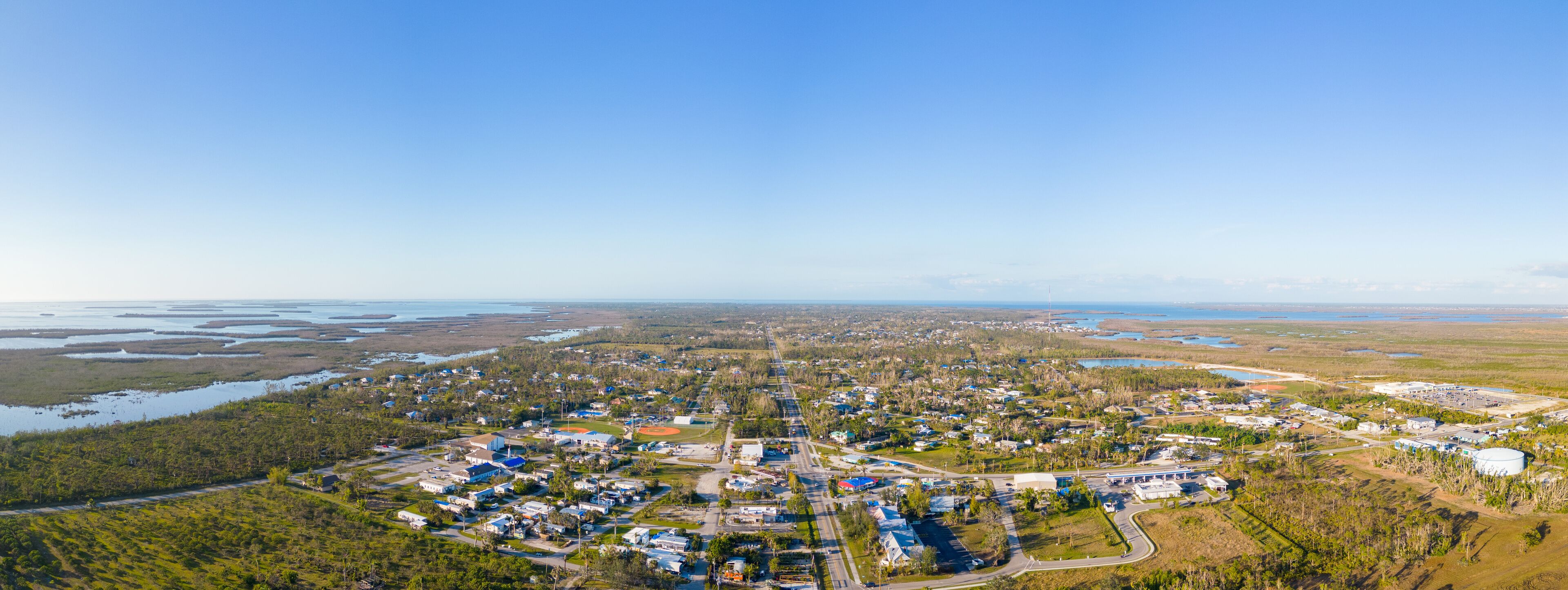 An aerial view of a coastal town with residential areas, a baseball field, and a large body of water.