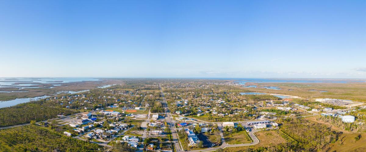 An aerial view of a coastal town with residential areas, a baseball field, and a large body of water.