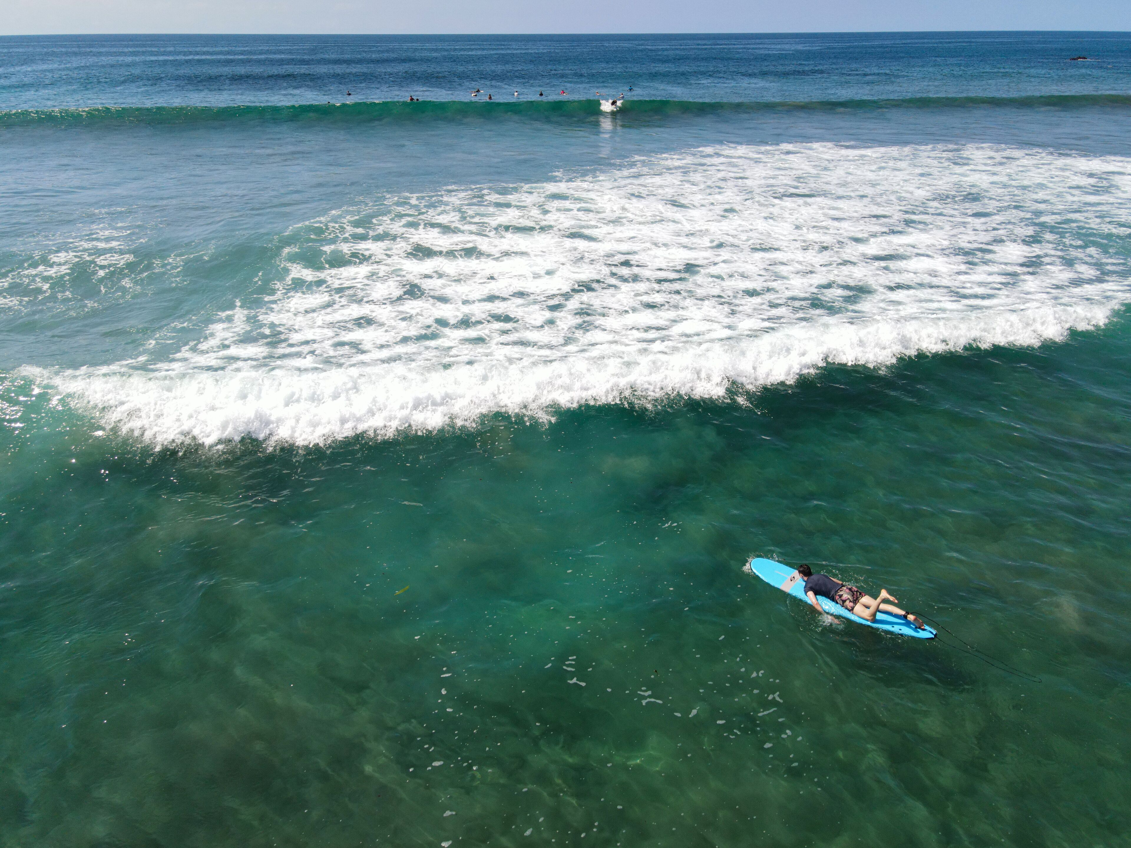 A clear blue ocean with a surfer on a blue surfboard.
