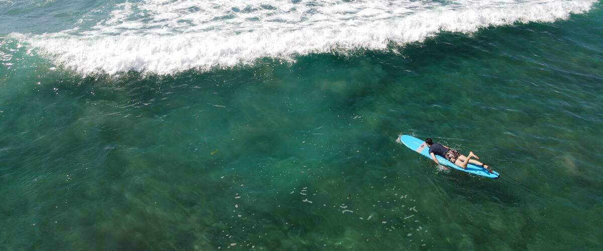 A clear blue ocean with a surfer on a blue surfboard.