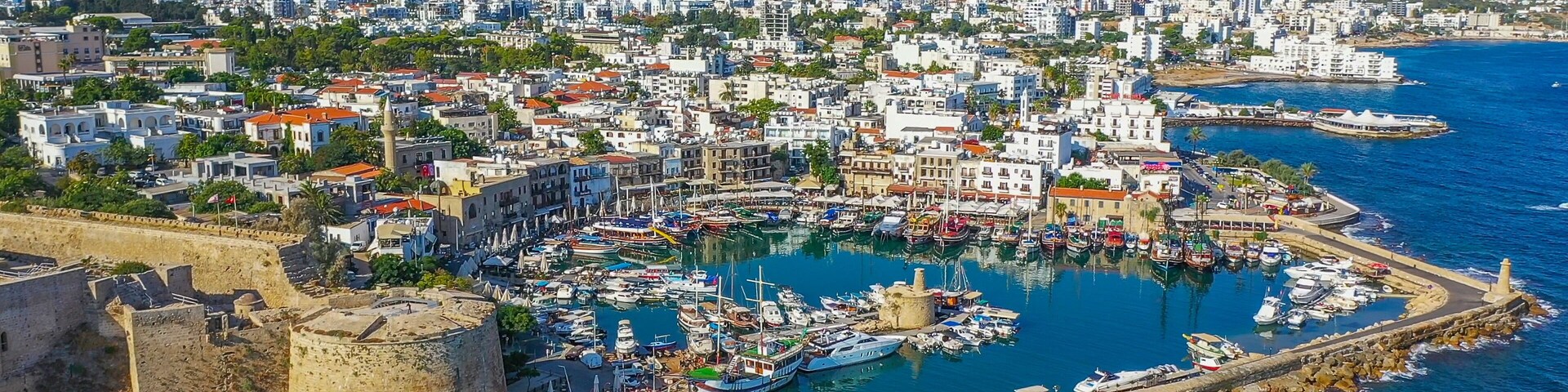 Un pueblo costero con un puerto, barcos y una fortaleza histórica.