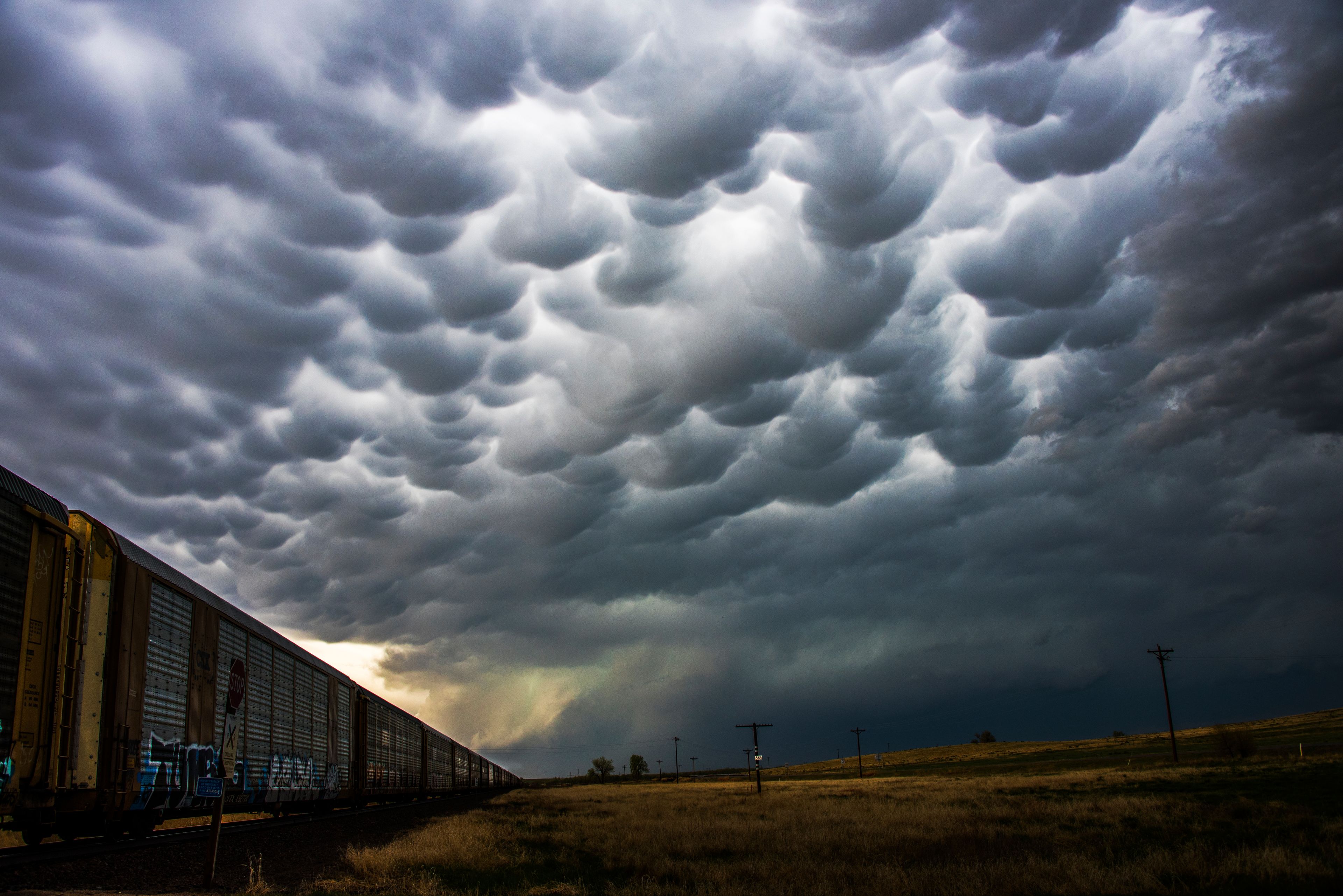 A train track with graffiti, a cloudy sky, and a grassy field.