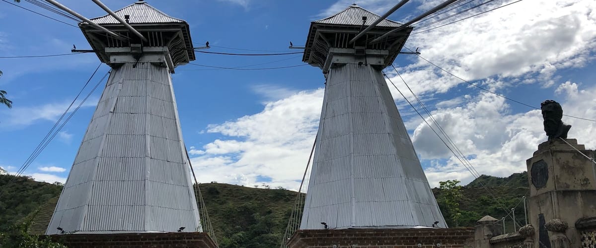 A suspension bridge with two towers and a brick building at the end.