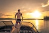 Un hombre en un bote al atardecer, con un lago y árboles a lo lejos.