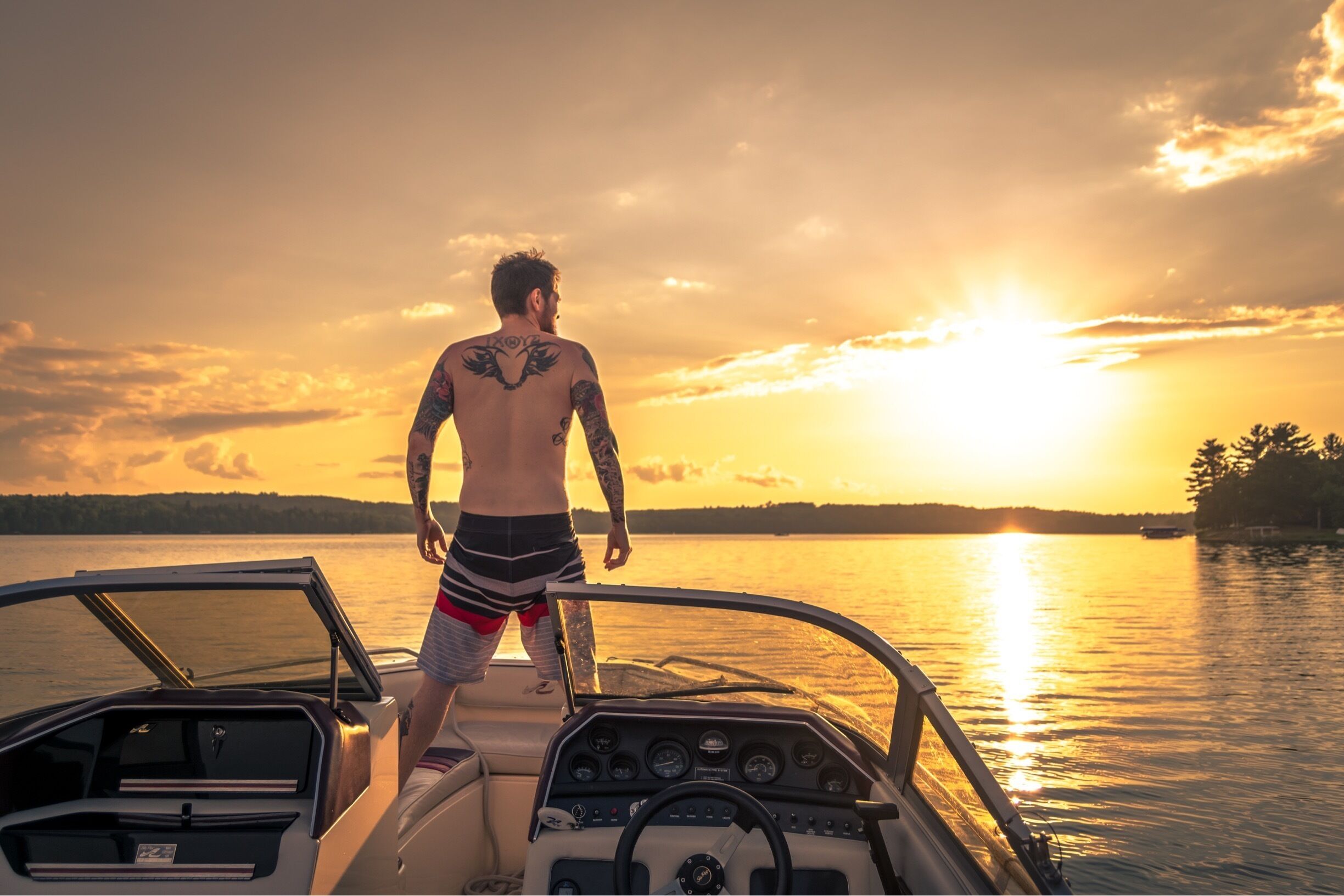 A man on a boat during sunset with a lake and distant trees.