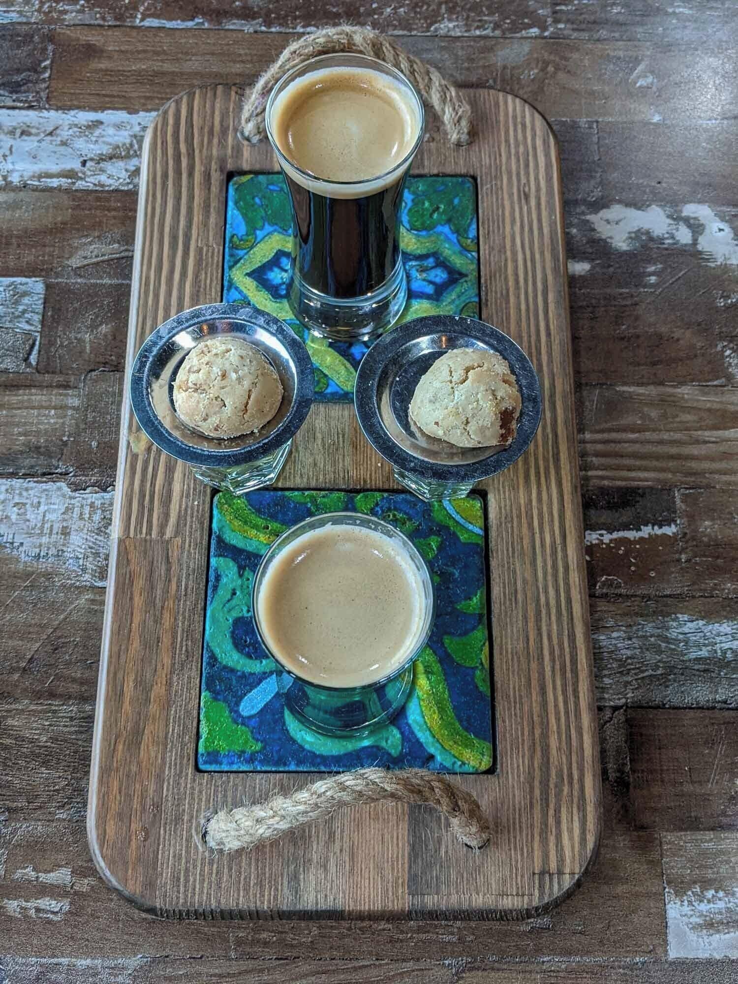 A wooden serving tray with three glasses of coffee and two cookies.