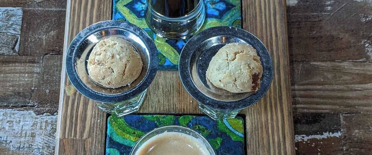A wooden serving tray with three glasses of coffee and two cookies.