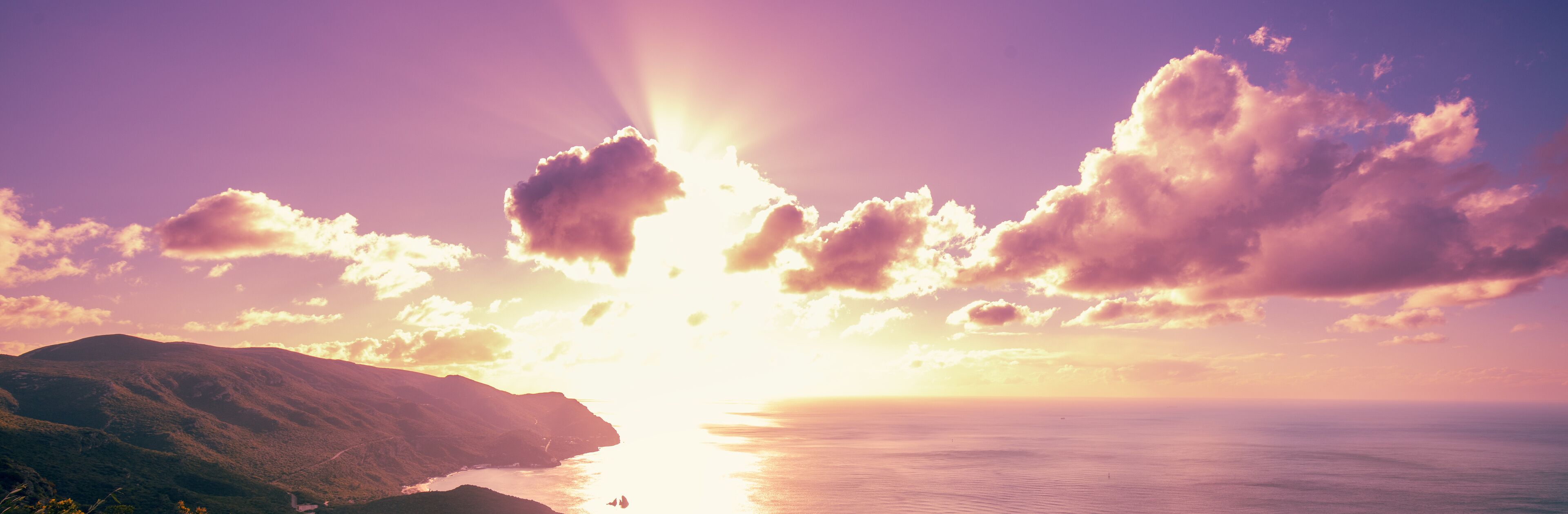 A sunset over a coastal landscape with mountains and a body of water.
