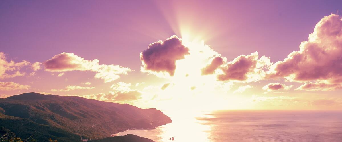 A sunset over a coastal landscape with mountains and a body of water.