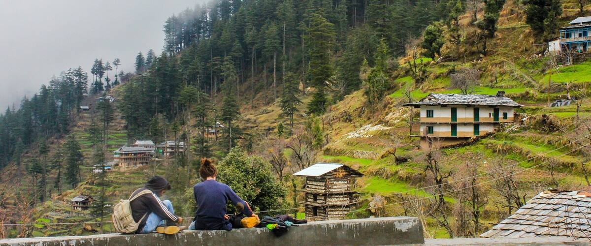 A mountainous landscape with terraced fields, traditional houses, and a person sitting on a ledge.