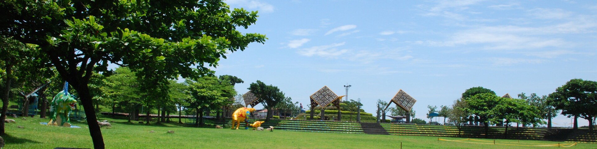 Un parque con césped verde, árboles y un parque infantil con un tobogán amarillo.
