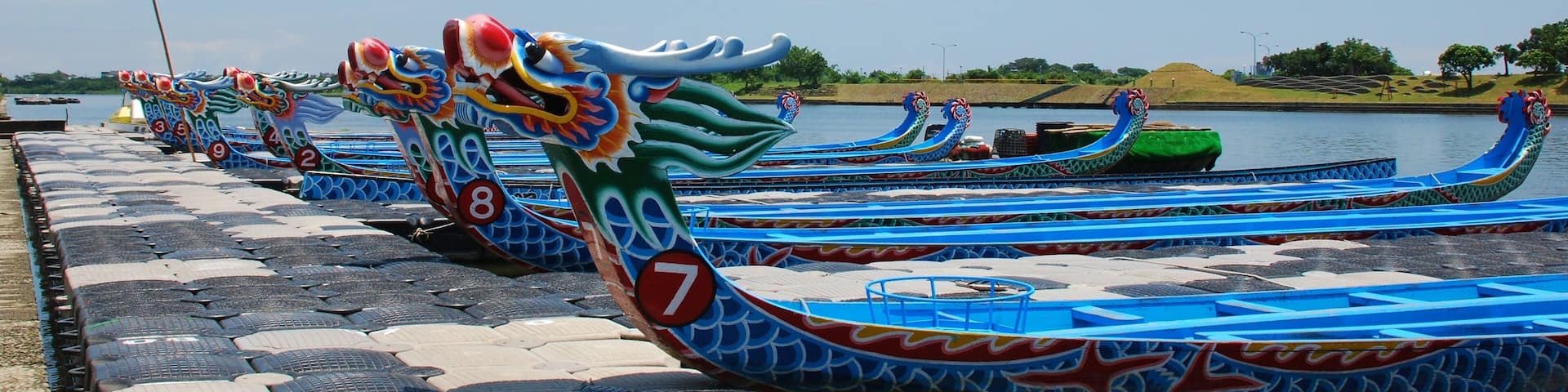 A row of dragon boats lined up on a dock by a calm river.
