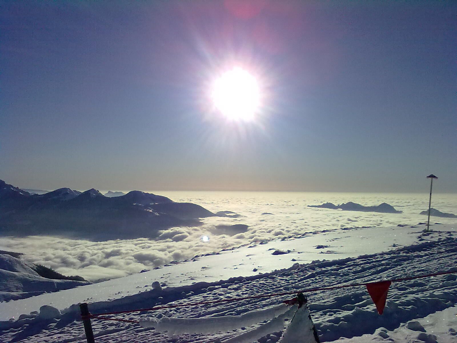 A snowy mountain landscape with a clear sky and the sun shining brightly.