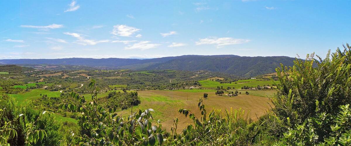 A lush valley with rolling hills, a stone wall, and distant mountains under a clear sky.