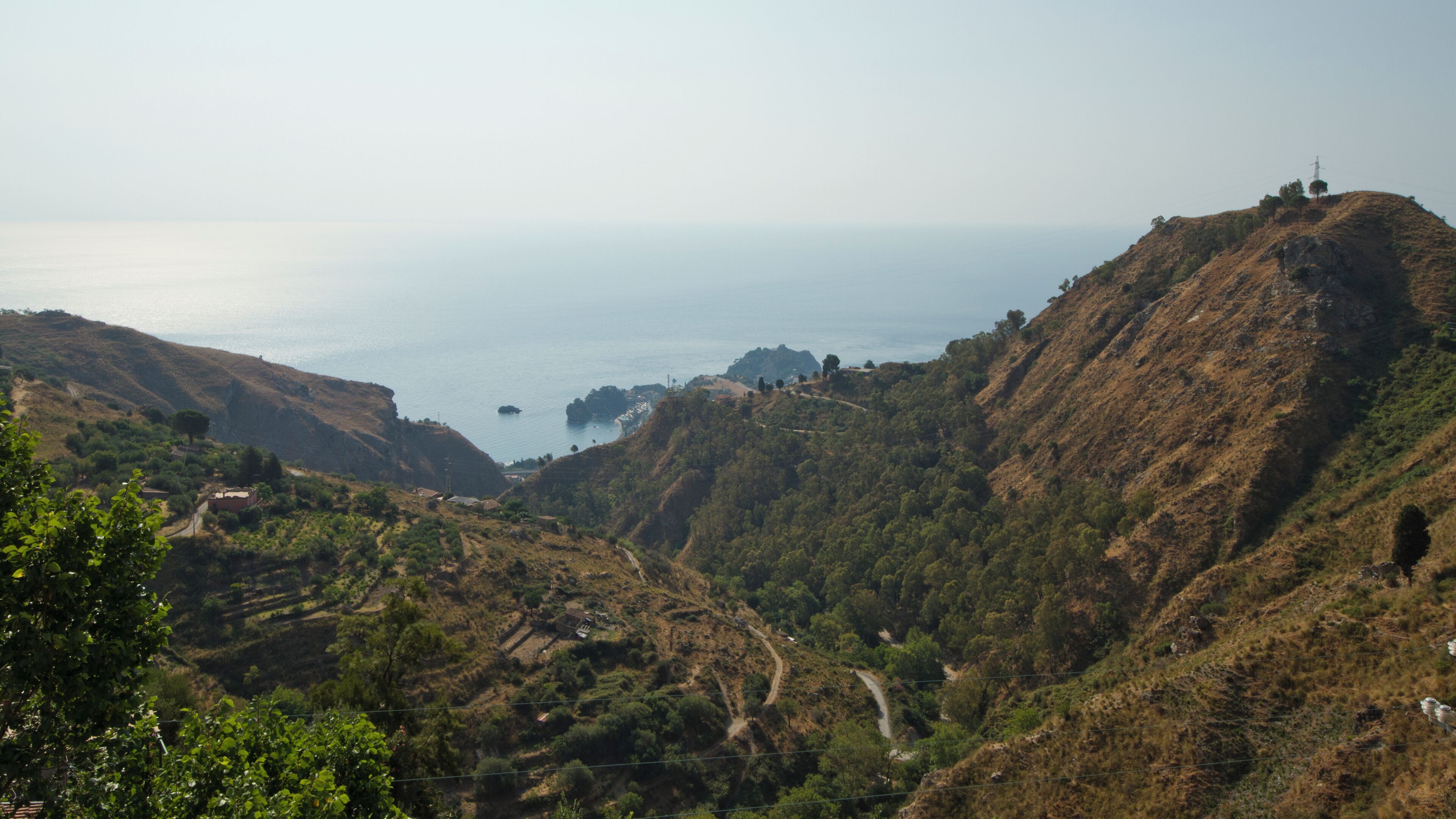 A coastal landscape with hills, a winding road, and a distant view of the sea.