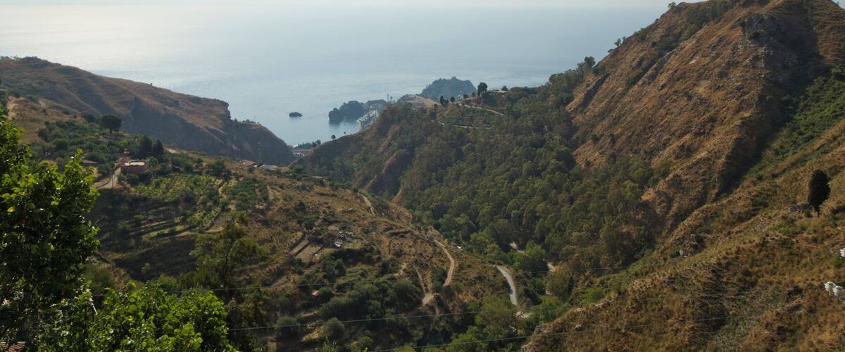 A coastal landscape with hills, a winding road, and a distant view of the sea.