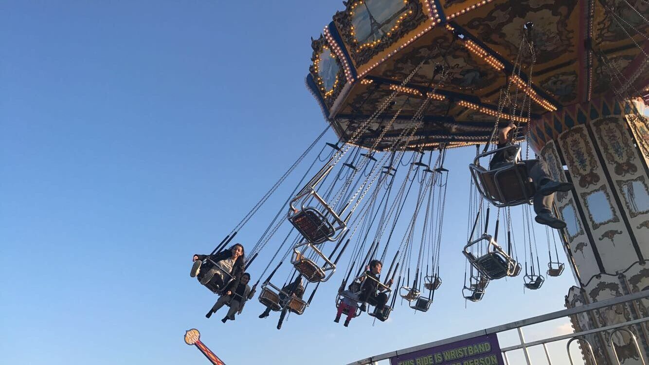 A carousel with multiple seats suspended by chains against a clear blue sky.