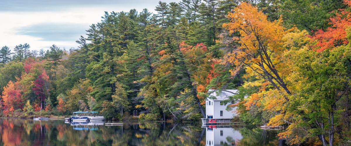 A lake surrounded by autumn-colored trees, a white house, and boats on the water.