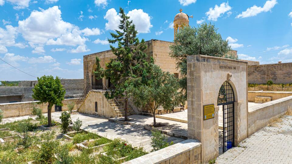 A historical building with a dome and arched entrance, surrounded by trees and stone walls.