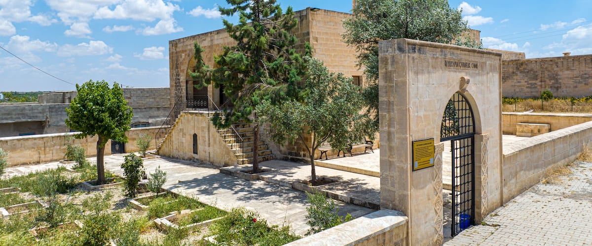 A historical building with a dome and arched entrance, surrounded by trees and stone walls.