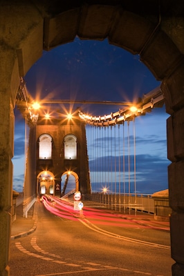 A bridge at dusk with illuminated lights and a red light trail from moving vehicles.