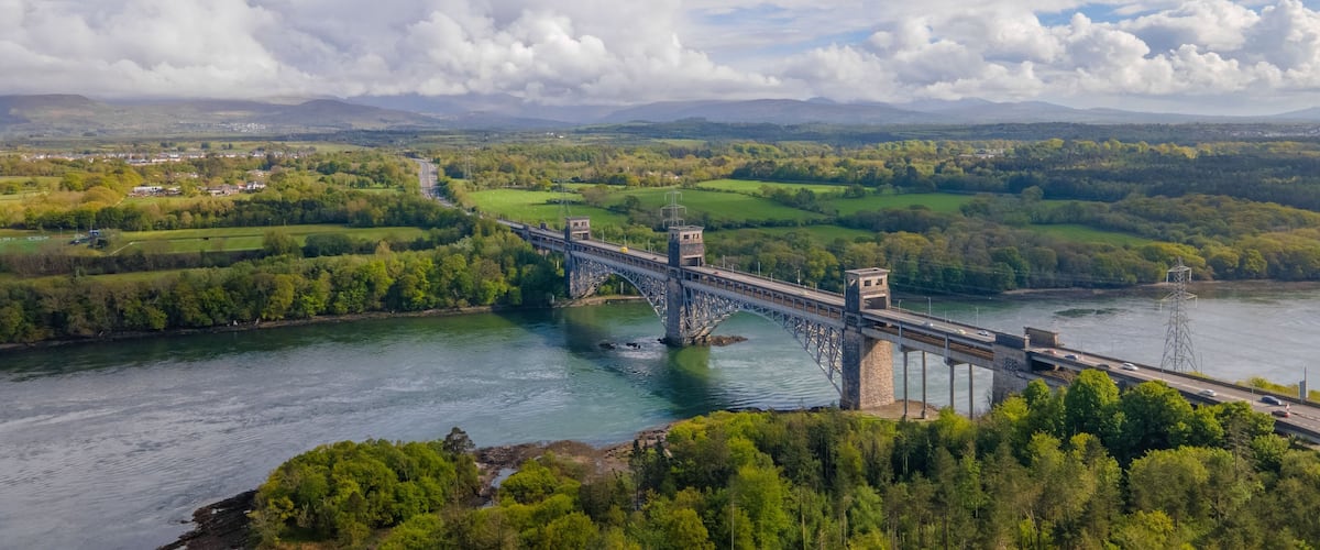 A bridge over a river with surrounding greenery and distant hills.