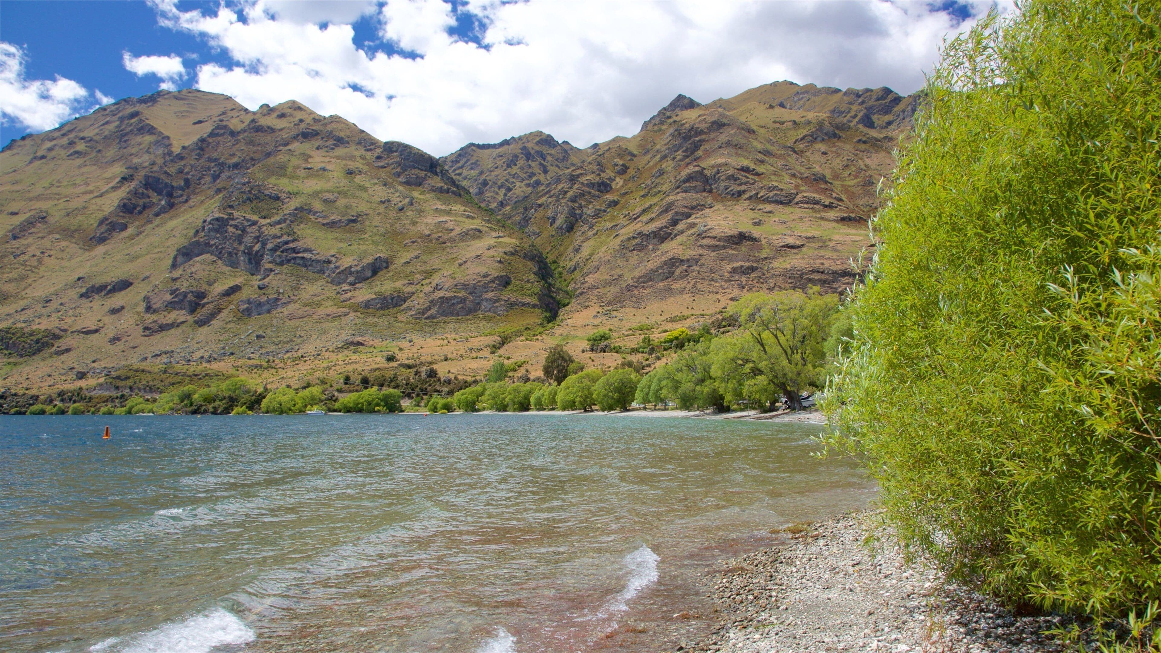 A lake with clear water, surrounded by mountains and greenery.