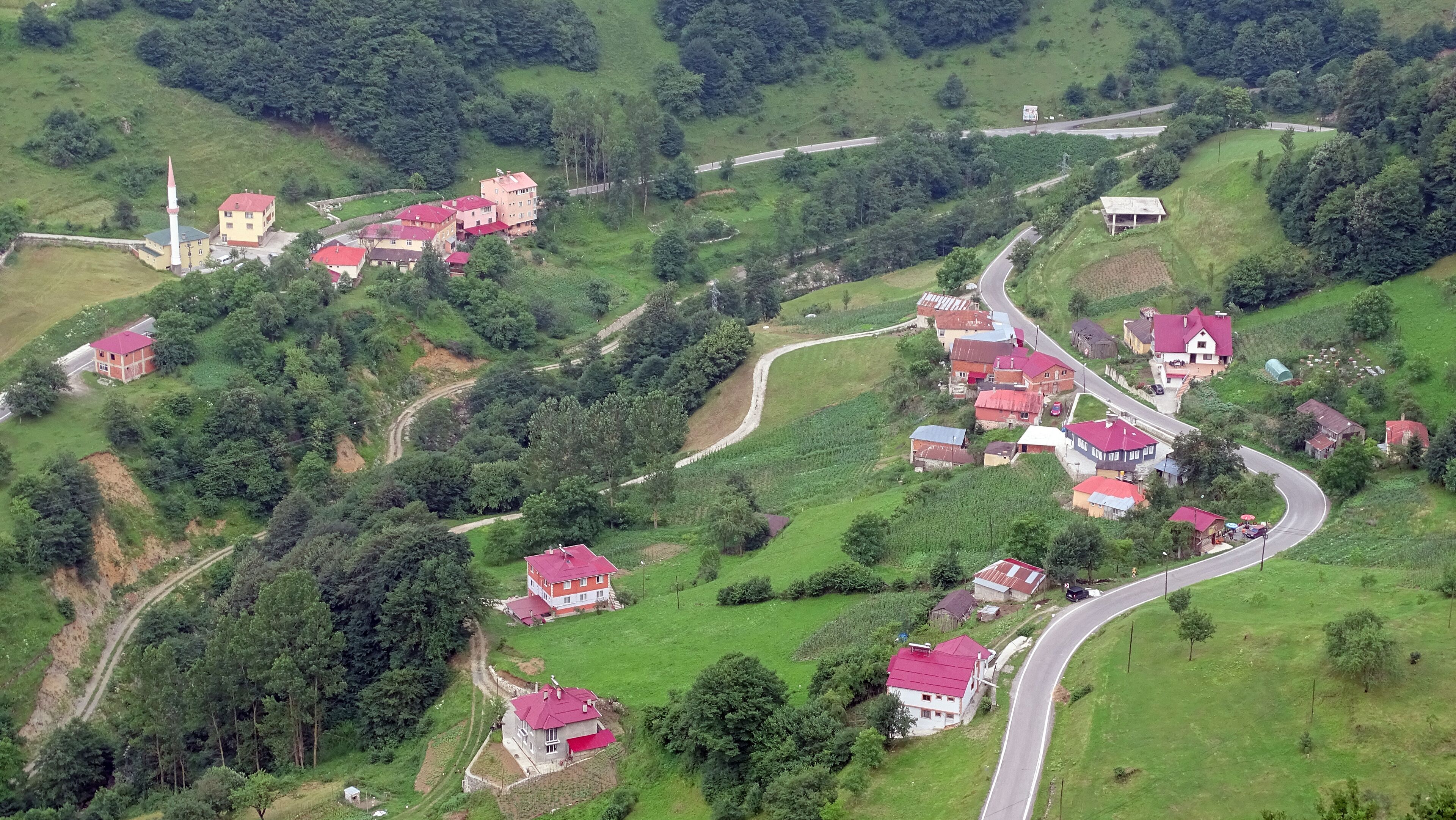 An aerial view of a hilly village with red-roofed houses, a church with a tall steeple, and winding roads.