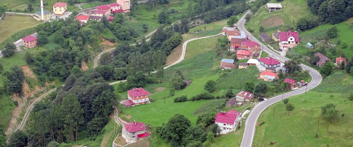 An aerial view of a hilly village with red-roofed houses, a church with a tall steeple, and winding roads.