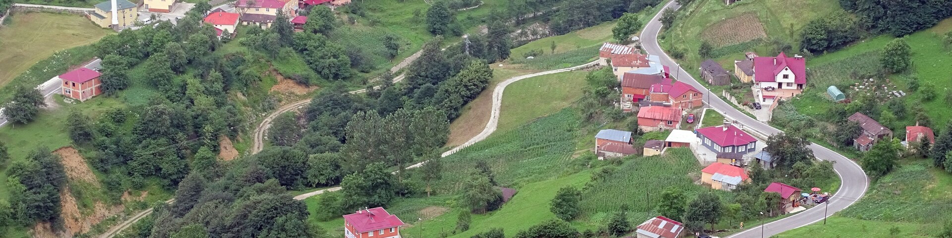 An aerial view of a hilly village with red-roofed houses, a church with a tall steeple, and winding roads.