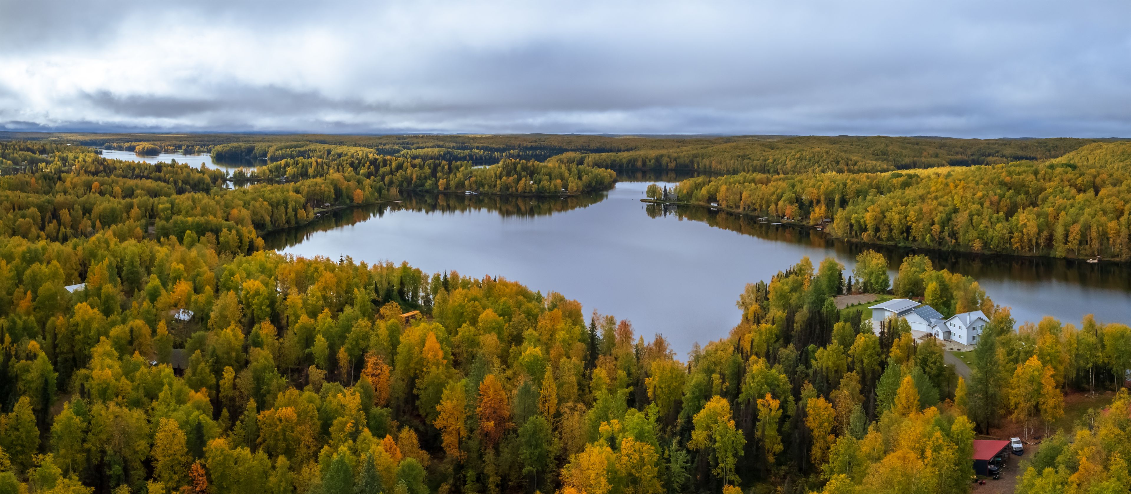 Un lac entouré d’arbres aux couleurs automnales, sous un ciel nuageux.