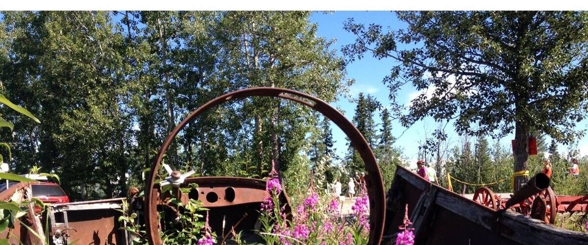 A rusty metal structure surrounded by wildflowers and trees.