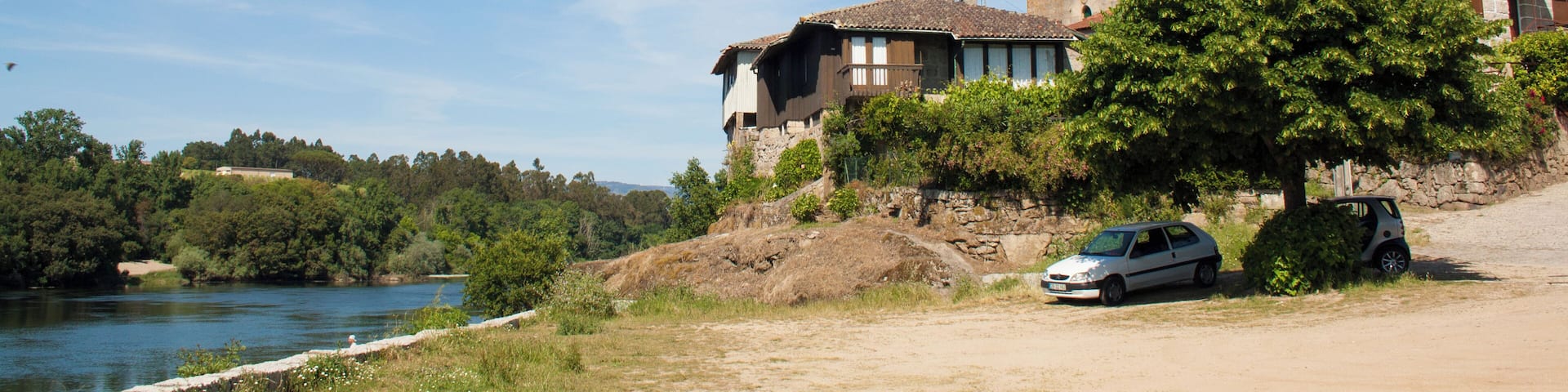 A historic tower, a river, and a car parked by the roadside.