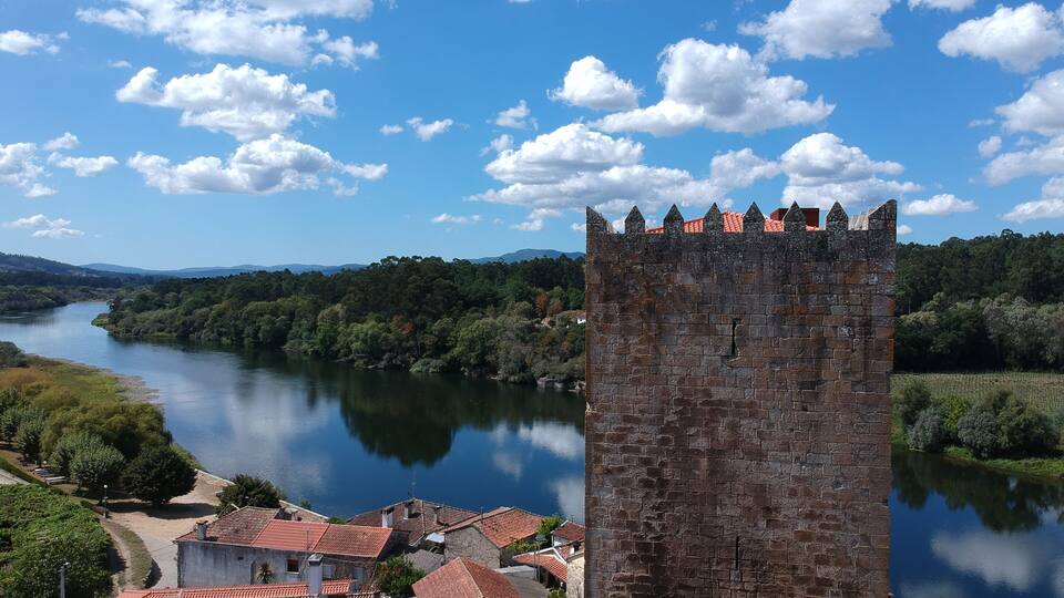 A castle overlooking a river, surrounded by greenery and a clear blue sky.